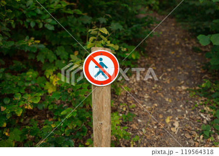 A round sign prohibiting entry into the forest. Shows a crossed-out person. The sign is in focus on the centre of the frame, and the blurred background is a forest green. Ojcowski park  119564318