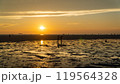 Group walking on beach during sunset, admiring red sky at dusk over water 119564328