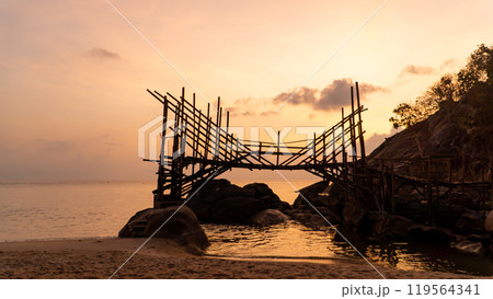 A wooden bridge spans a serene water body at sunset 119564341