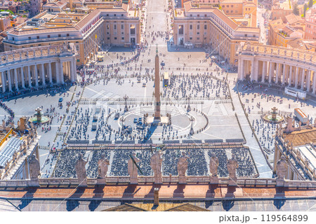 Visitors gather in Saint Peter's Square, surrounded by impressive architecture, enjoying a sunny day in front of the majestic St. Peter's Basilica with vibrant atmosphere and historical significance. 119564899