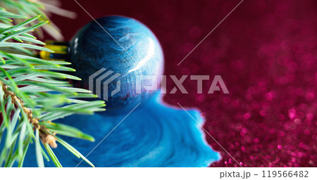 Xmas background. Paint bauble. Green pine tree branch shiny blue color ink pouring over sparkling round ball on pink bokeh light free space. 119566482