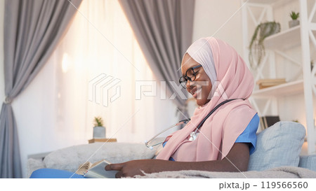 Healthcare learning. Medical education. Nurse course. Cheerful woman intern student reading research book studying disease on sofa at clinic. 119566560