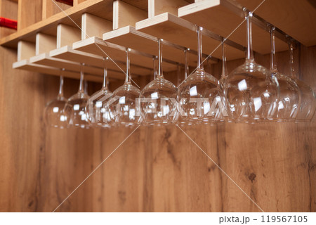 a row of wine glasses hanging from a wooden rack a row of wine glasses hanging from a wooden rack 119567105
