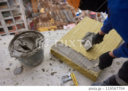 A construction worker is applying mortar on insulation board at a building site A construction worker is applying mortar on insulation board at a building site 119567704