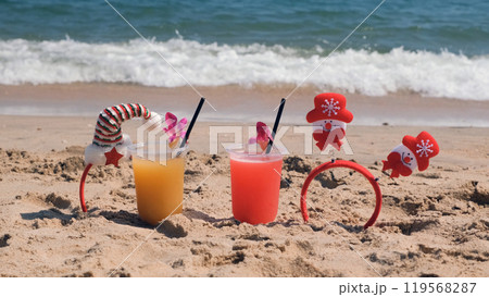 Colorful fruit cocktails with Christmas decorations on a warm sandy beach, celebrating a tropical winter holiday 119568287