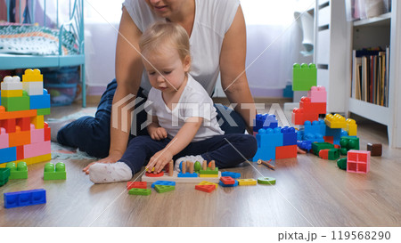 Loving mother and baby daughter play together with colorful wooden toys in their cozy nursery at home 119568290