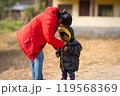 Mother helping baby keeping warm wearing warm clothes standing outdoors. 119568369