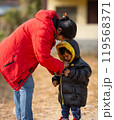 Mother helping baby keeping warm wearing warm clothes standing outdoors. 119568371