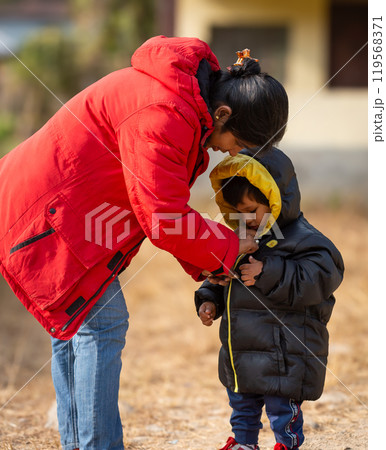 Mother helping baby keeping warm wearing warm clothes standing outdoors. Mother helping baby keeping warm wearing warm clothes standing outdoors. 119568371