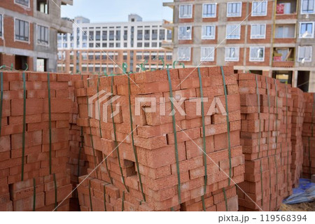 Stack of bricks on wooden pallet in front of building under construction Stack of bricks on wooden pallet in front of building under construction 119568394