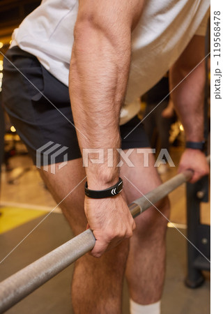 A man is strengthening and improving his fitness by lifting a barbell in the gym 119568478