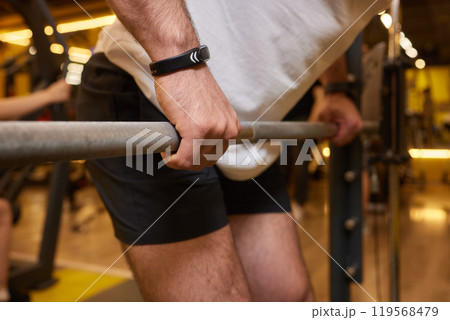 A man is strengthening and improving his fitness by lifting a barbell in the gym A man is strengthening and improving his fitness by lifting a barbell in the gym 119568479
