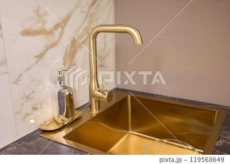 A gold faucet on a bathroom sink with a soap bottle A gold faucet on a bathroom sink with a soap bottle 119568649