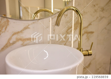 A gold faucet on a bathroom sink with a soap bottle A gold faucet on a bathroom sink with a soap bottle 119568659