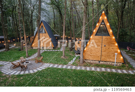 Modern wooden A-frame cabins in forest with outdoor seating and fire pit area, relaxation time Modern wooden A-frame cabins in forest with outdoor seating and fire pit area, relaxation time 119569463