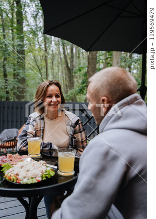 Couple enjoying food and beer outdoors, sharing laughter and moments of connection on forest terrace Couple enjoying food and beer outdoors, sharing laughter and moments of connection on forest terrace 119569479