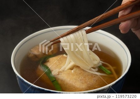 きつねうどん　巾着きつねうどん 油揚げに詰めたうどんを箸で持ち上げる 119573220