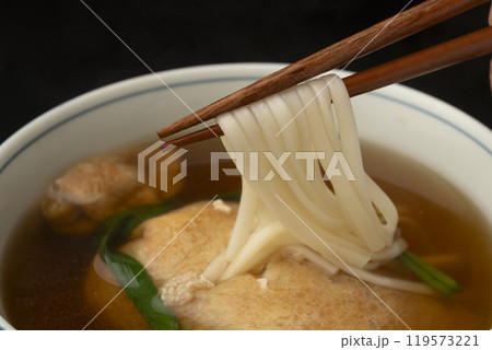 きつねうどん　巾着きつねうどん 油揚げに詰めたうどんを箸で持ち上げる 119573221