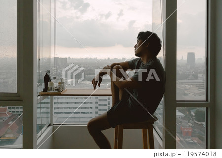 Introvert lonely man sitting hugging his knees looking out. 119574018