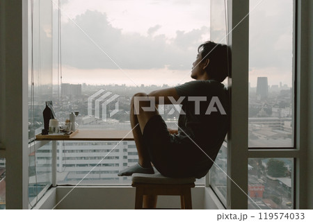 Introvert lonely man sitting at the windows enjoy being alone in apartment. Introvert lonely man sitting at the windows enjoy being alone in apartment. 119574033