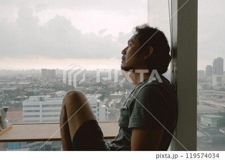 Introvert lonely man sitting at the windows enjoy being alone in apartment. 119574034