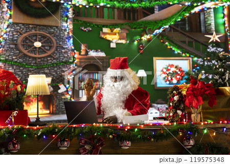 African american Santa Claus chatting with parents and kids before Christmas, gathering wishes for toys as gifts. Modern Saint Nicholas using technology to make children happy, holiday spirit. 119575348