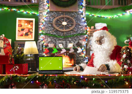 Santa Claus sitting next to copy space screen on device and reading letters from children around the world. Old man Saint Nicholas spreading his festive cheer for the holiday period. 119575375