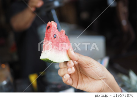 A Fresh Slice of Watermelon Being Held by a Hand Set Against a Vibrant and Lively Background A Fresh Slice of Watermelon Being Held by a Hand Set Against a Vibrant and Lively Background 119575876