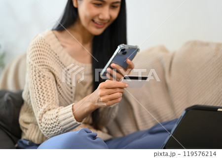 Happy young woman using credit card for online shopping on her smartphone Happy young woman using credit card for online shopping on her smartphone 119576214