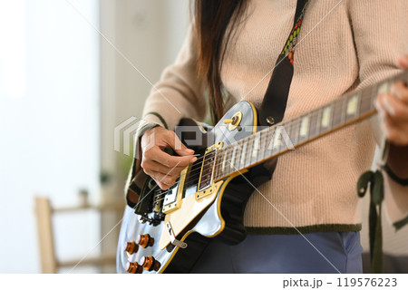 Close up of female musician strumming electric guitar strings Close up of female musician strumming electric guitar strings 119576223