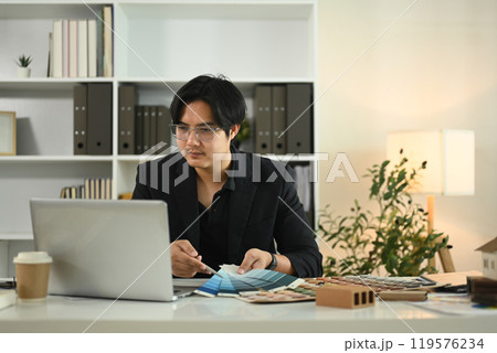 Architect using laptop and reviewing color samples for a project at his office Architect using laptop and reviewing color samples for a project at his office 119576234