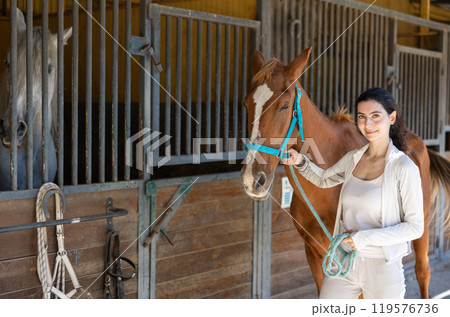 Young woman leads horse out of stable Young woman leads horse out of stable 119576736