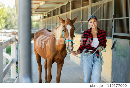 Young woman leads horse out of stable Young woman leads horse out of stable 119577000