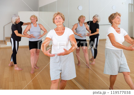 Aged women exercising ballet dance moves with trainer Aged women exercising ballet dance moves with trainer 119577038