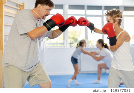 Boy and dad are boxing in gym, father helps child to work out force of blow. Boy and dad are boxing in gym, father helps child to work out force of blow. 119577081