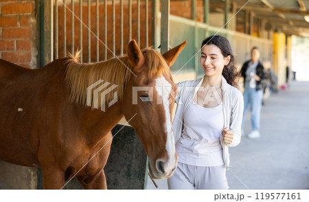 Young woman leads horse out of stable Young woman leads horse out of stable 119577161