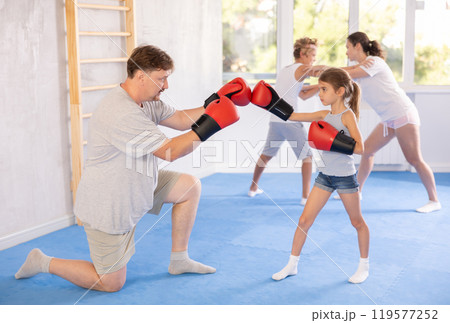 Girl and dad are boxing in gym, father helps child to work out force of blow. Girl and dad are boxing in gym, father helps child to work out force of blow. 119577252