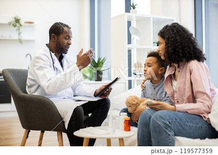 Doctor assists concerned mother with examination of her son 119577359