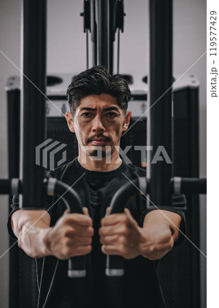 スポーツジムで上半身を鍛える40代男性 119577429
