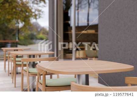 A minimalist contemporary cafe features an outdoor patio area with a row of wooden tables. 119577641