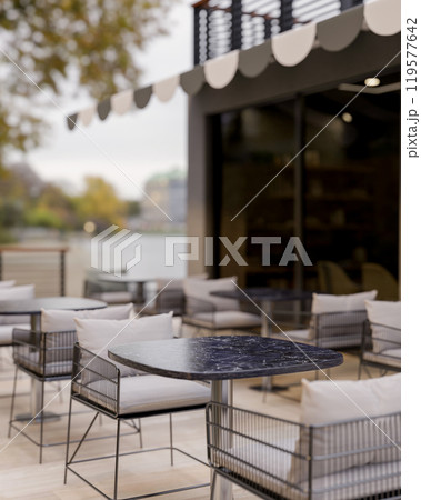 A modern cafe or restaurant features an outdoor patio area with rows of tables and armchairs. 119577642