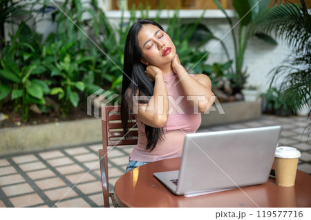 A woman is working remotely from a coffee shop, feeling tired and experiencing neck pain. A woman is working remotely from a coffee shop, feeling tired and experiencing neck pain. 119577716