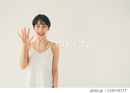 白い背景の前でキャミソール姿の若い女性が手のひらを見せるシーン 119578177