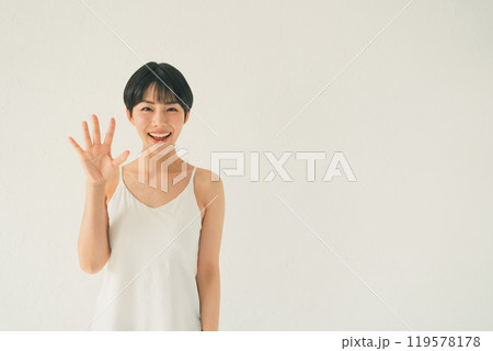 白い背景の前でキャミソール姿の若い女性が手のひらを見せるシーン 白い背景の前でキャミソール姿の若い女性が手のひらを見せるシーン 119578178