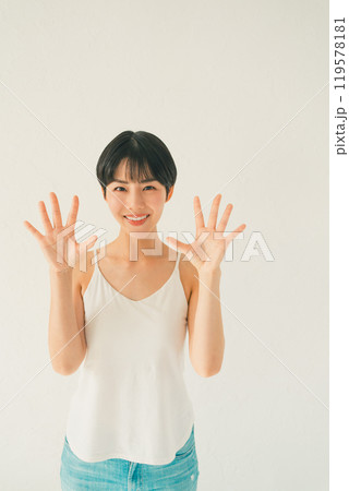 白い背景の前でキャミソール姿の若い女性が手のひらを見せるシーン 白い背景の前でキャミソール姿の若い女性が手のひらを見せるシーン 119578181
