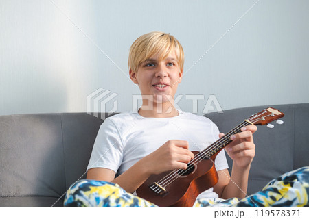 Happy boy playing ukulele while relaxing on sofa. Joy and music concepts. 119578371