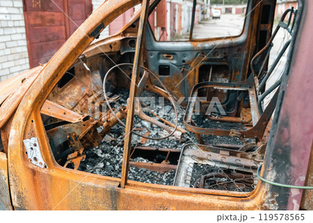 Rusty burnt out car in an abandoned backyard showing steering wheel and seats 119578565