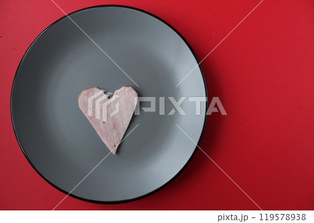 Still life breakfast for Valentine's Day Heart of ham sausage on a gray plate on a red bright background with a copy of the space 119578938