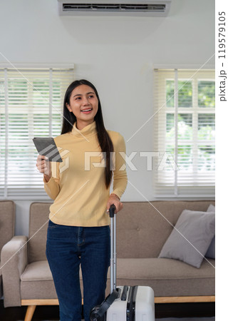 Young Woman Prepares for International Travel with Suitcase and Passport in Modern Living Room Setting 119579105