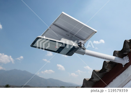 Mini solar cell panel and hd floodlight panal installed together under house eaves to store and use the power from the sunlight with street light and bulbs at night, sunset background, soft focus. Mini solar cell panel and hd floodlight panal installed together under house eaves to store and use the power from the sunlight with street light and bulbs at night, sunset background, soft focus. 119579359